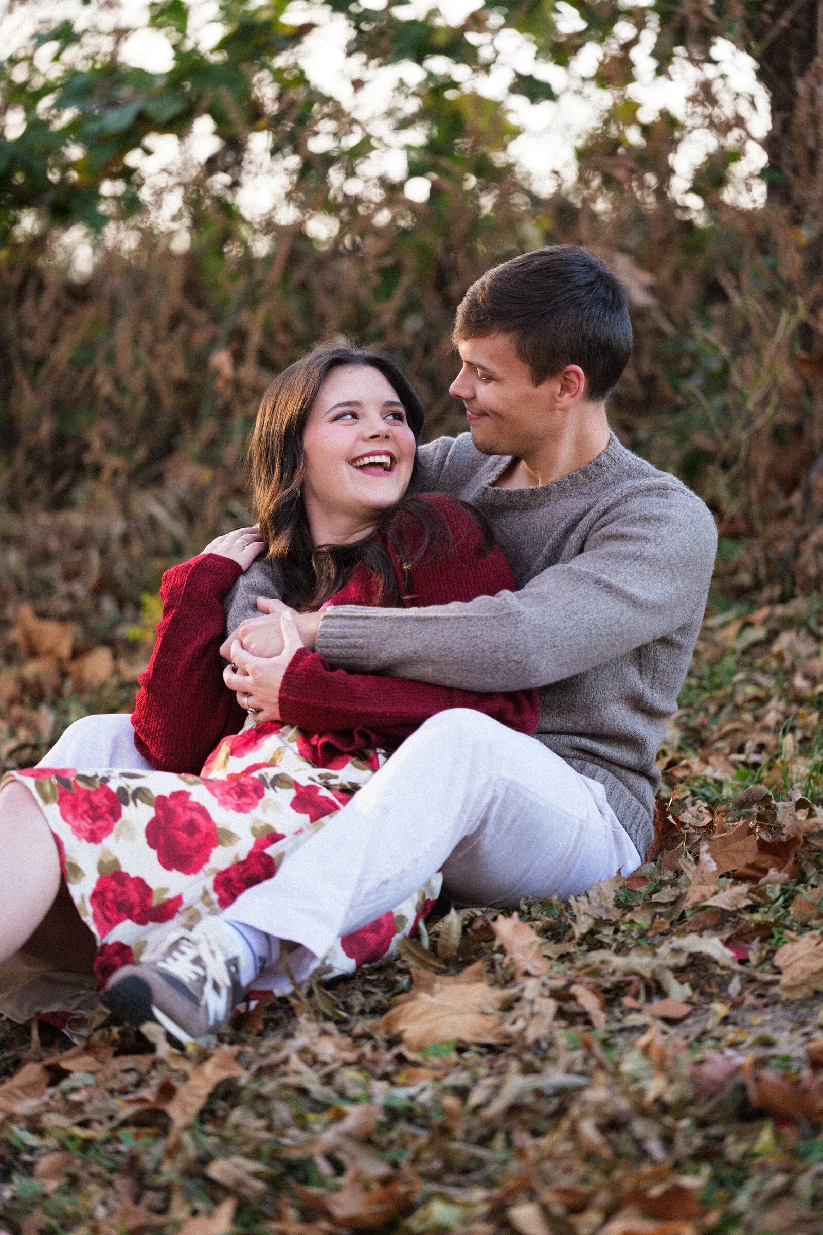 A couple sitting together in autumn leaves, laughing