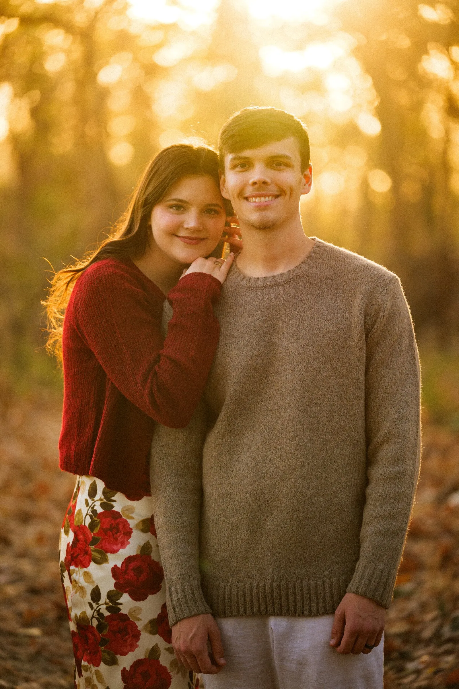 A couple standing close in golden woods, autumn light behind them