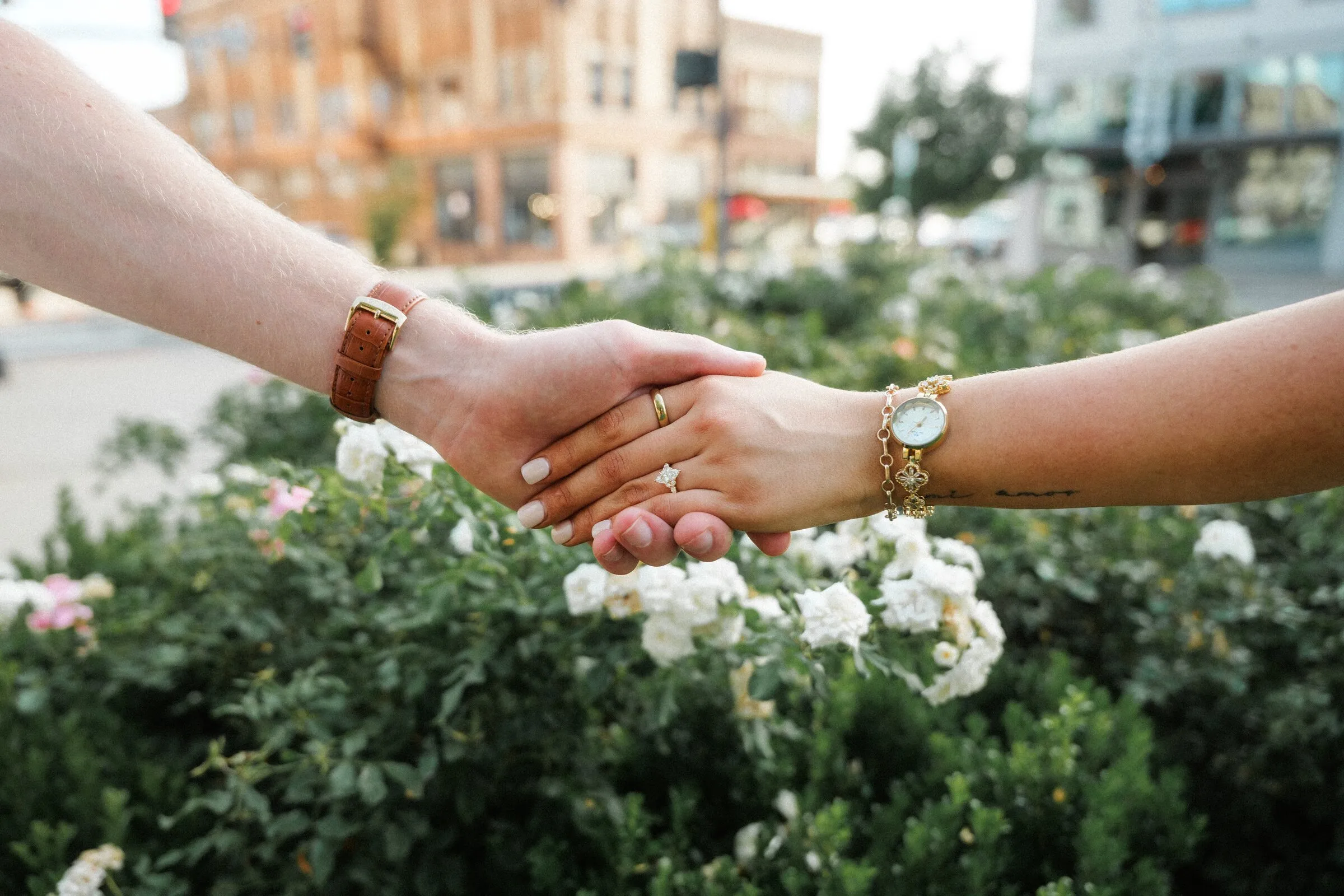 Two hands clasped over white roses on a downtown street