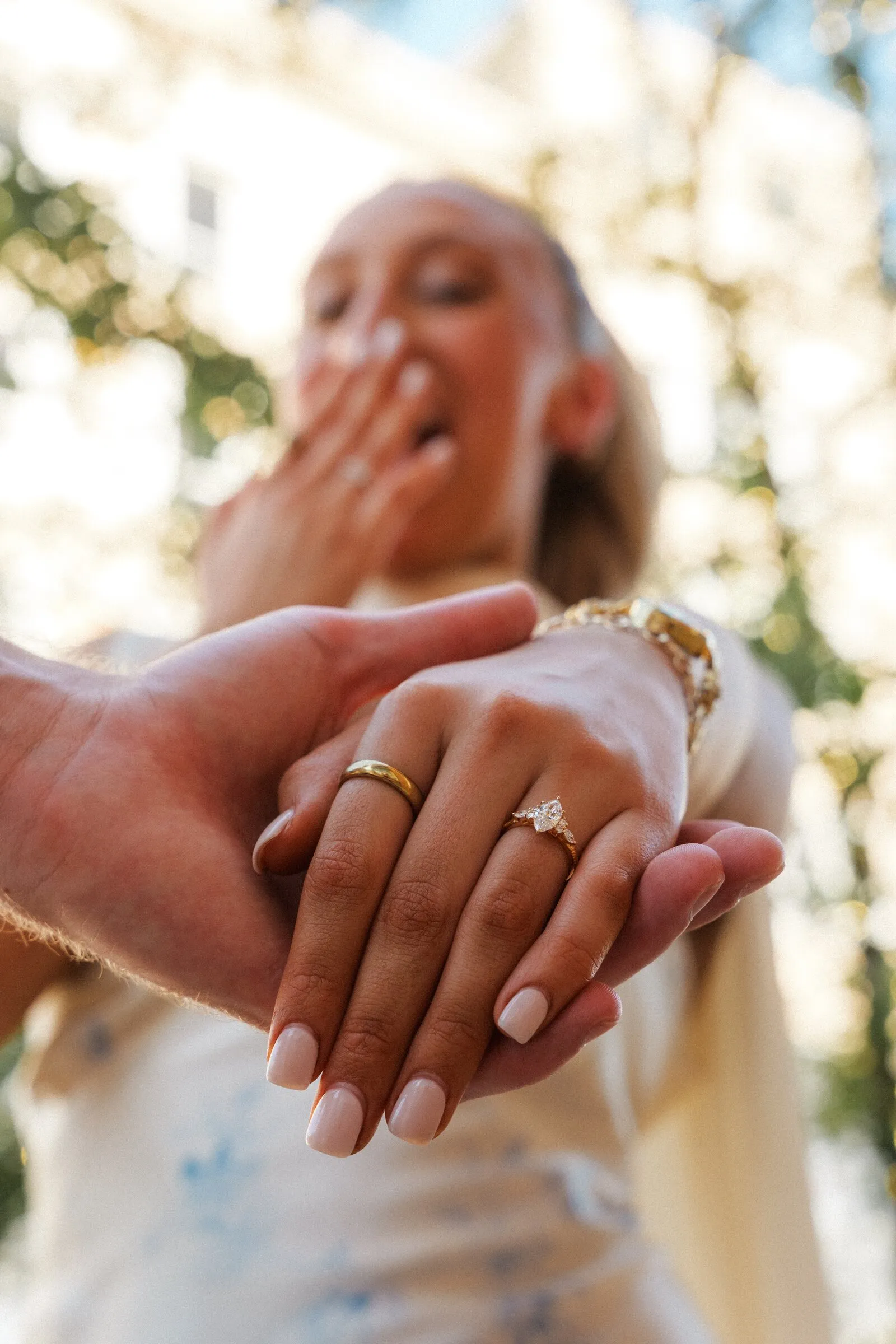 Close-up of an engagement ring on an outstretched hand, the bride-to-be laughing behind