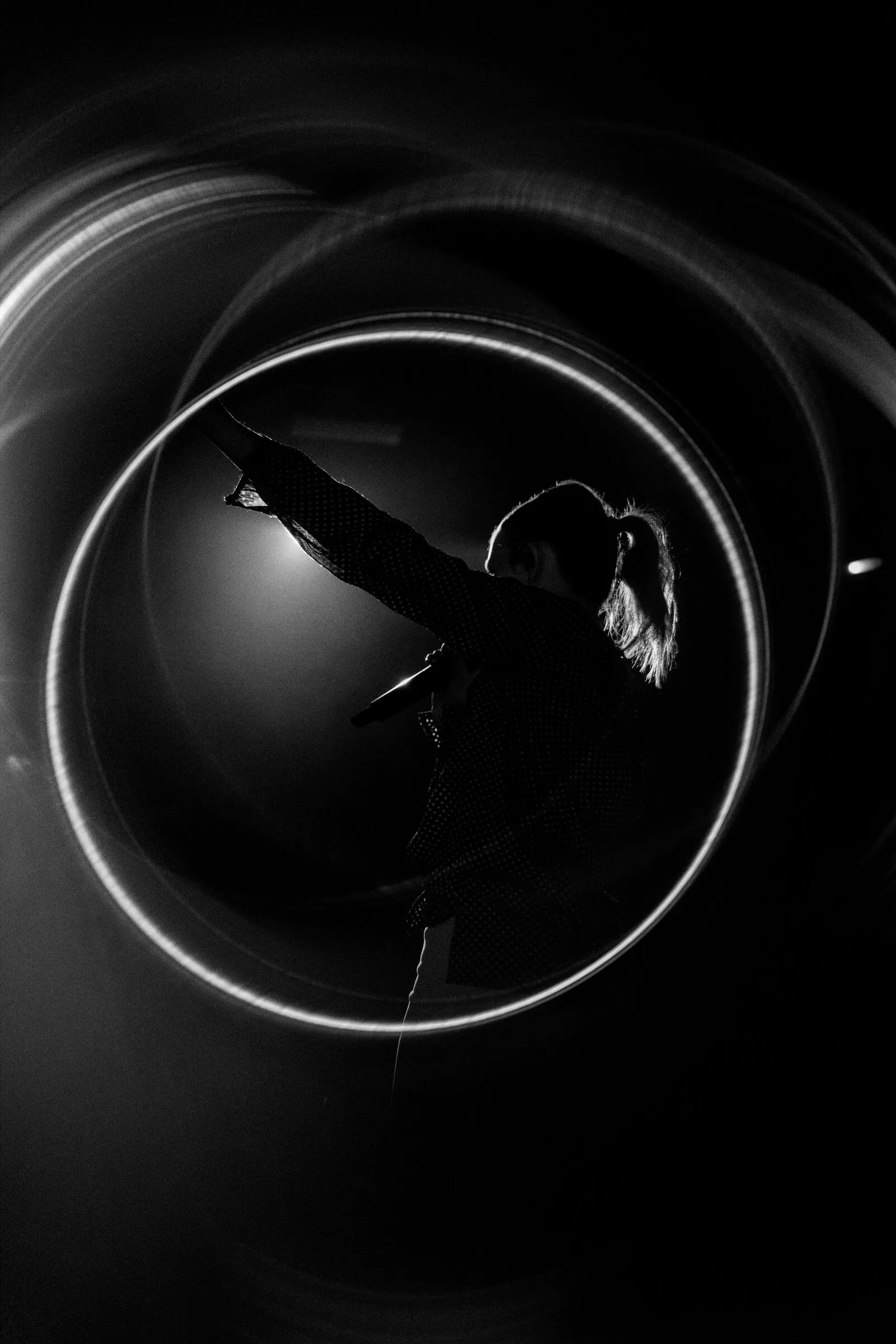 A performer silhouetted inside a thin ring of light, black and white