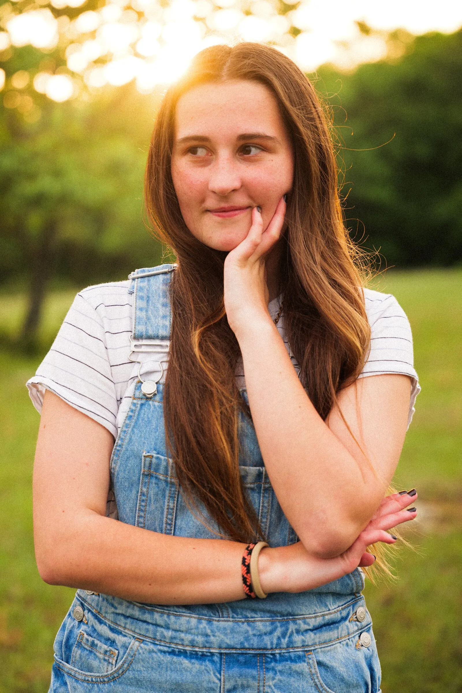 A senior in denim overalls smiling in golden-hour light