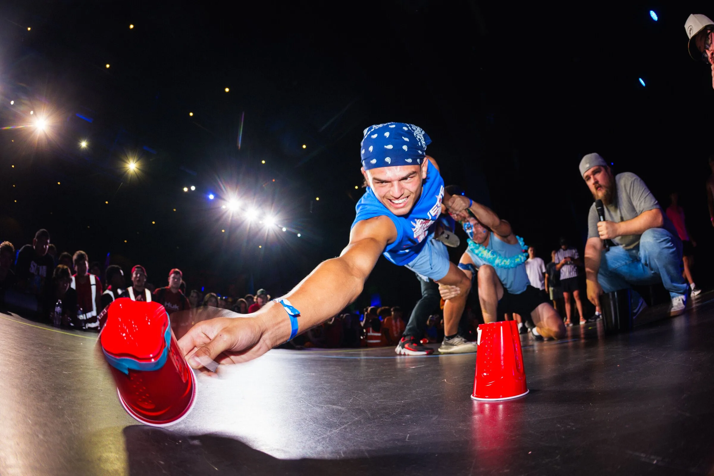 Students racing to flip red cups on a lit stage during a youth event game