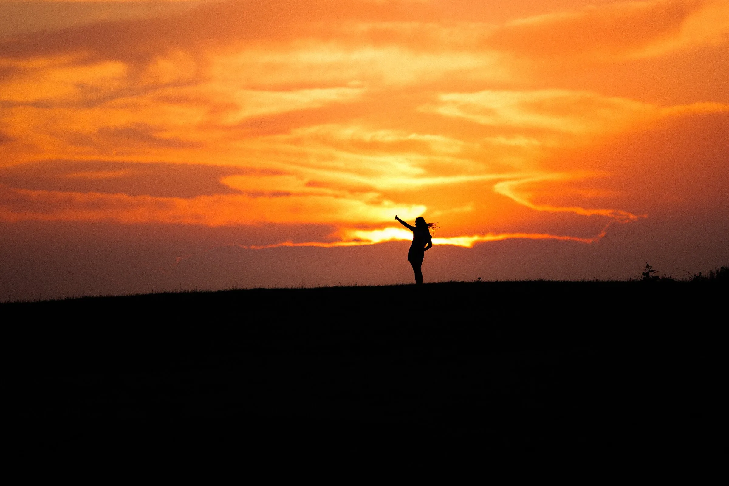 A lone figure on a ridge, arms out, against an orange Oklahoma sunset