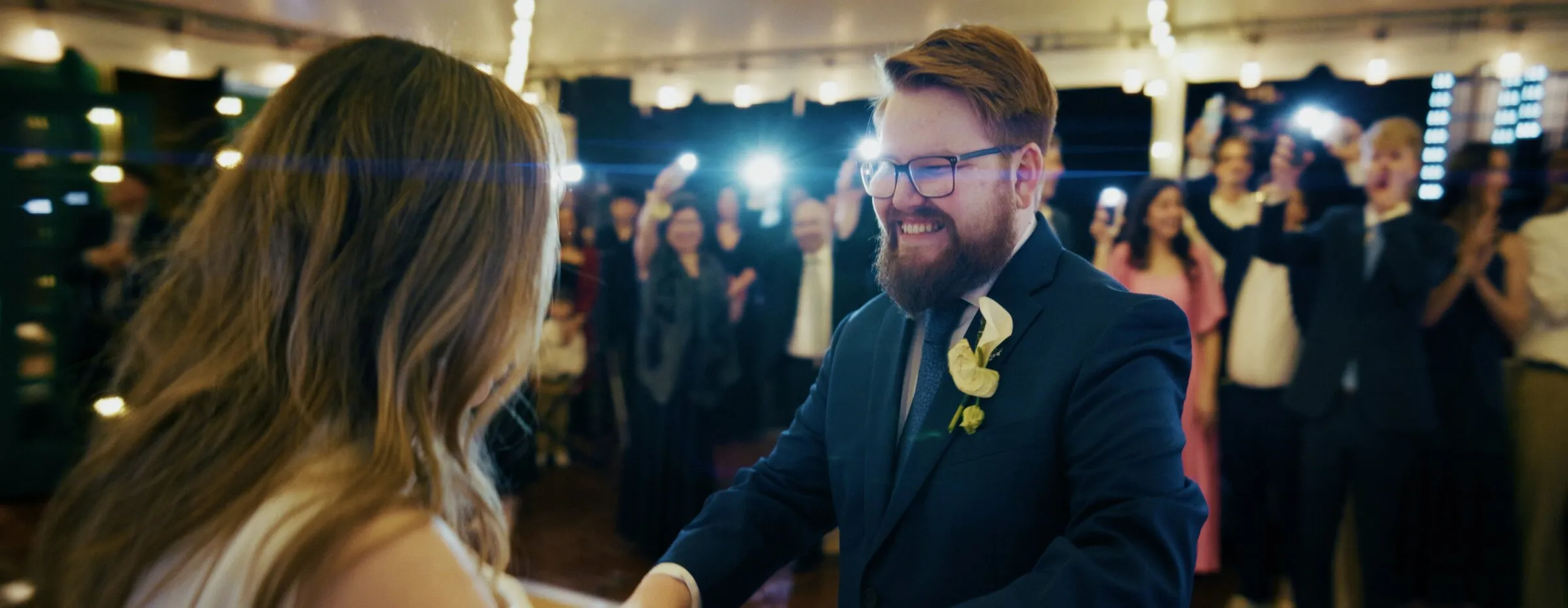 Bride and groom dancing as guests hold up phone lights around them