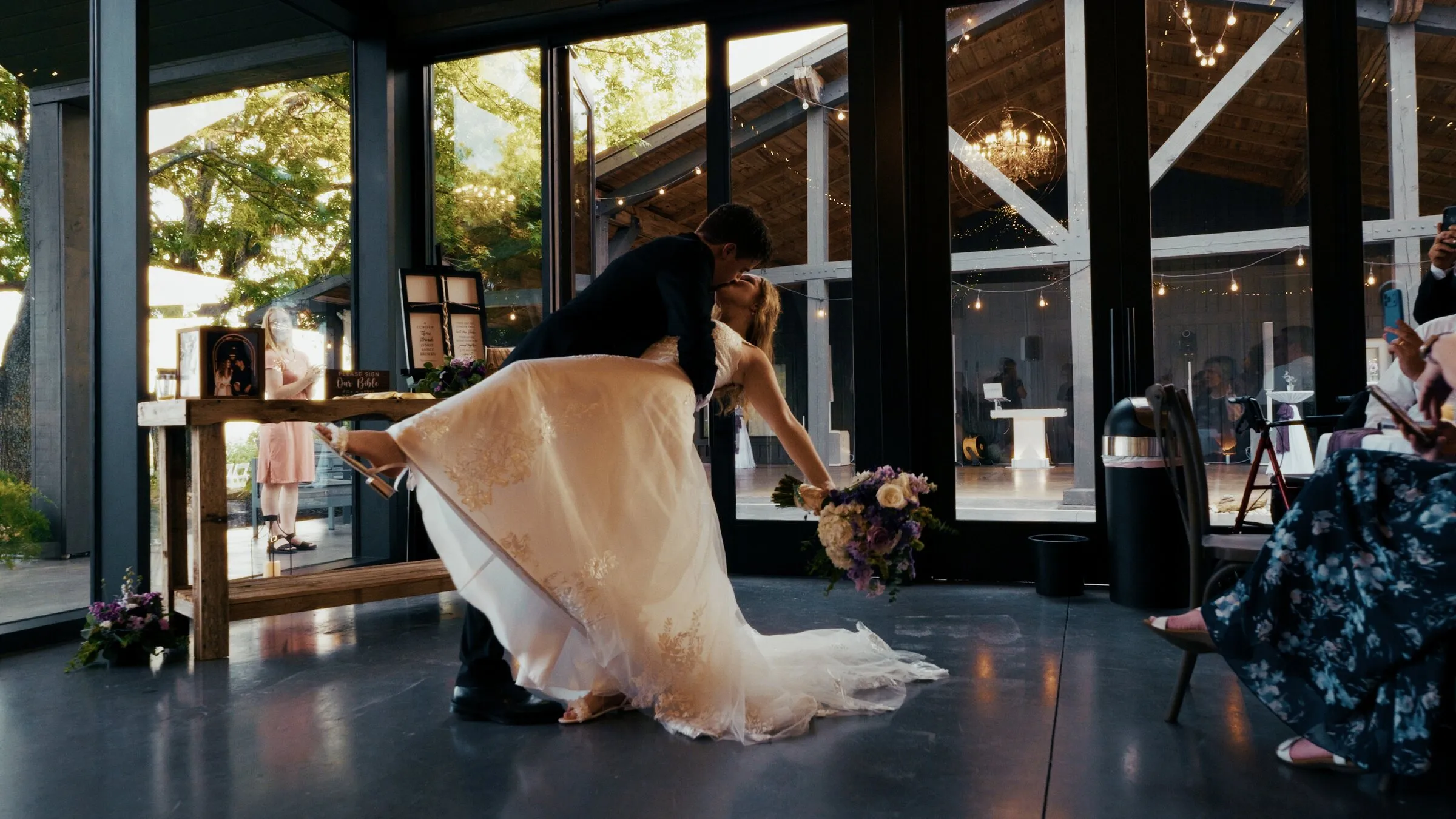 Groom dipping the bride on the dance floor of a glass-walled reception hall