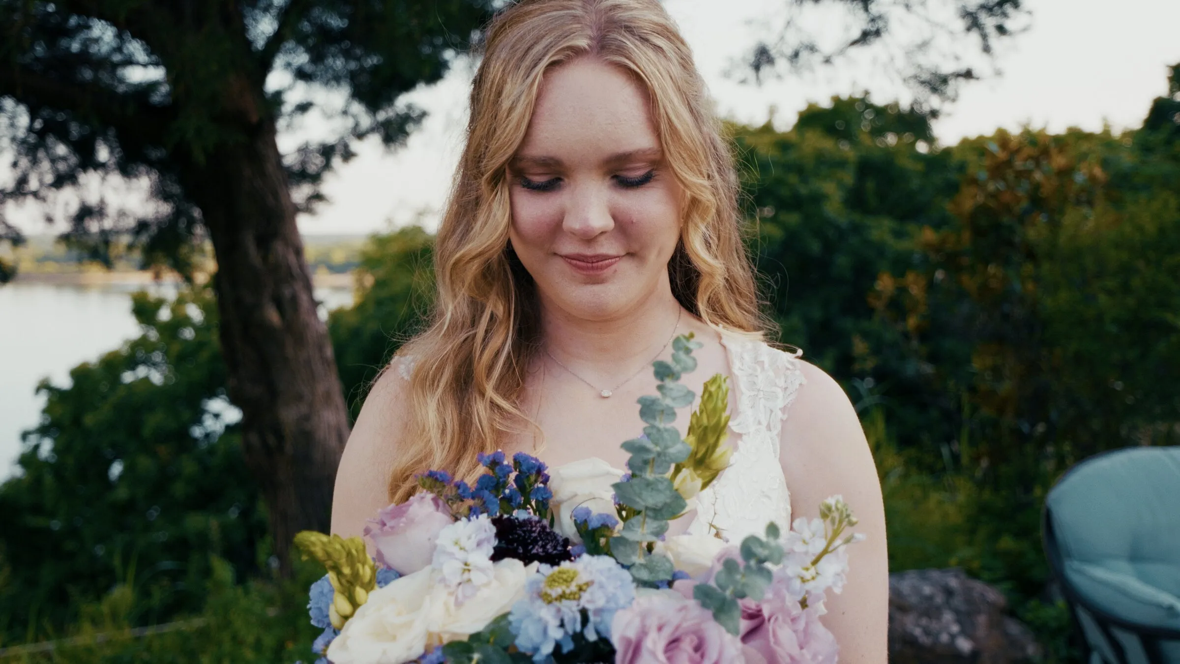 A bride looking down at her bouquet of lavender and white flowers in golden light