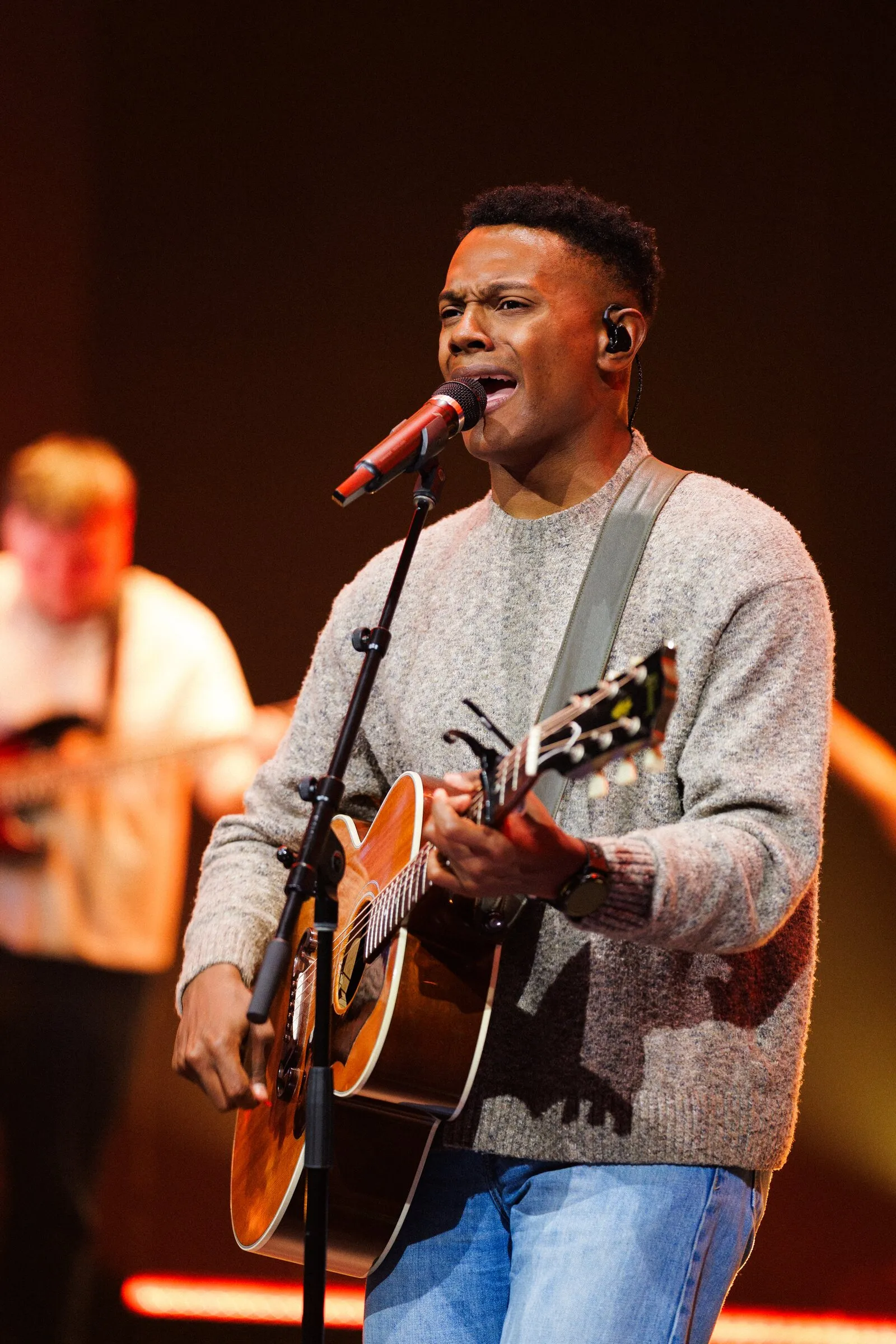 A worship leader singing and playing acoustic guitar on stage